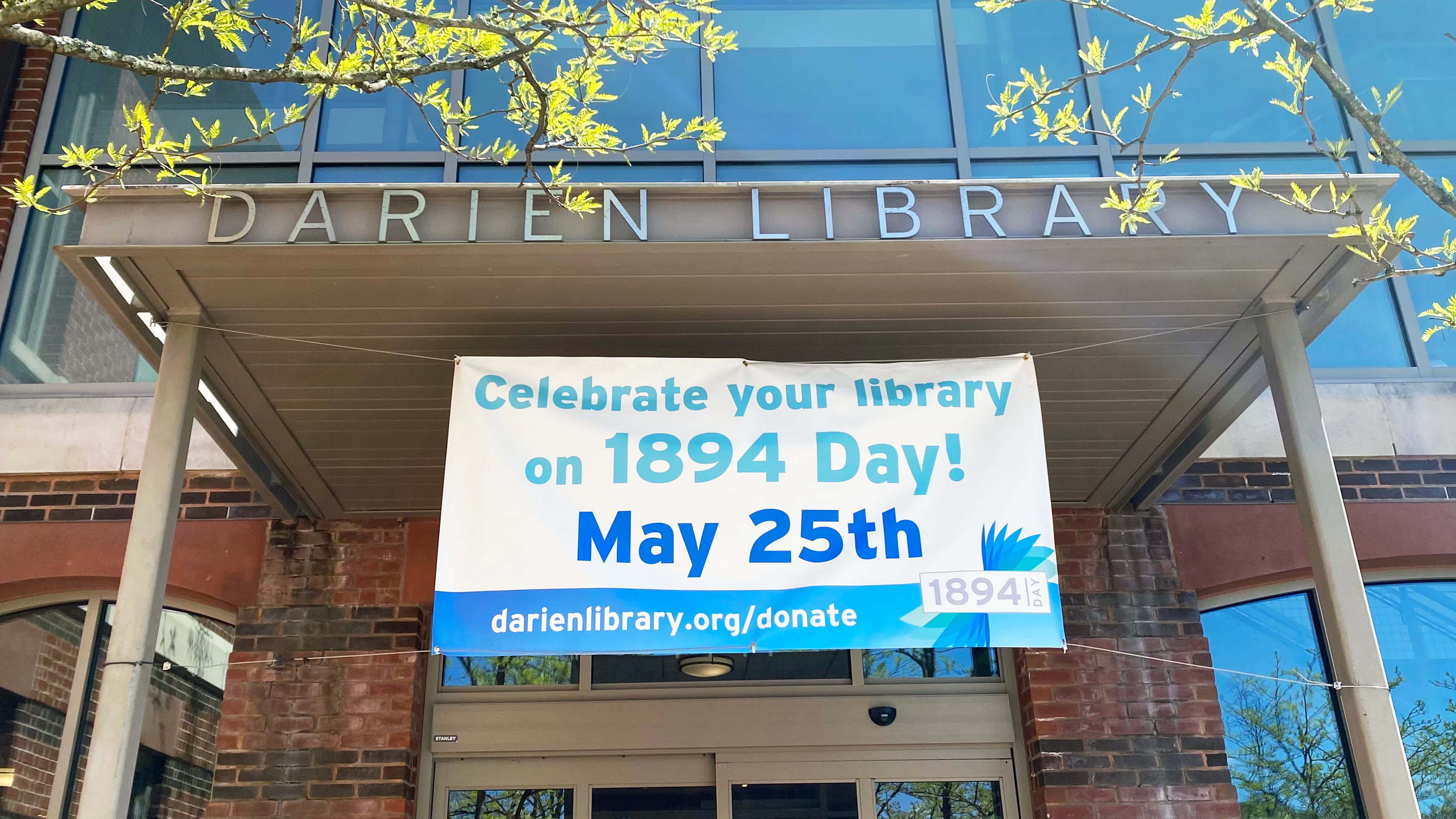 A banner under a sign reading "Darien Library" reads: "Celebrate your library on 1894 Day! May 25th!" darienlibrary.org/donate
