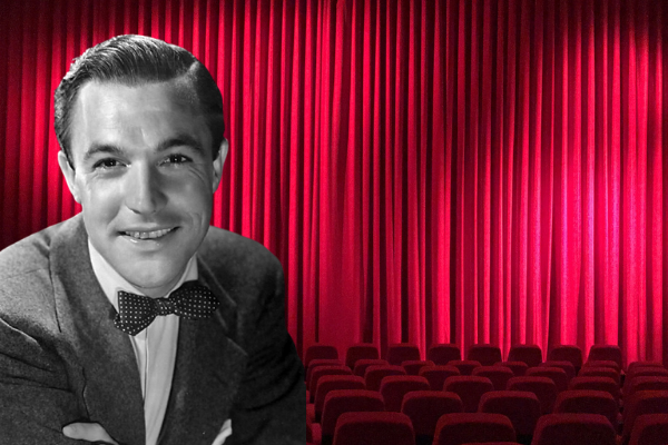 Black and white image of actor, Gene Kelly in front of red velvet curtain