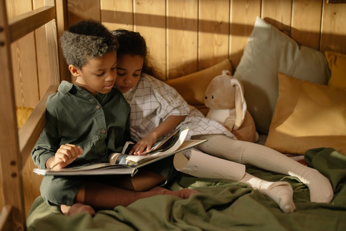 Two children snuggle up together while reading a book together.