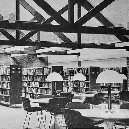 Library bookcases in the background with impressive overhead structural work. Tables are in the foreground.