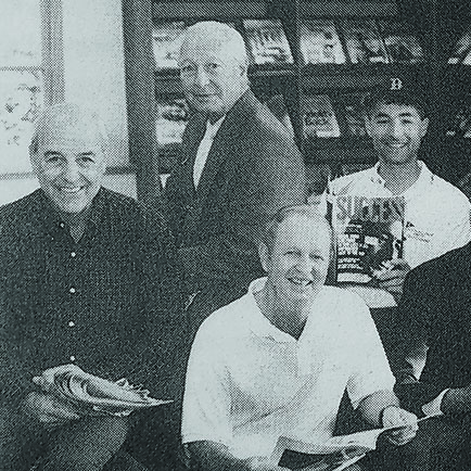 Four men sitting together holding magazines while smiling for the camera..