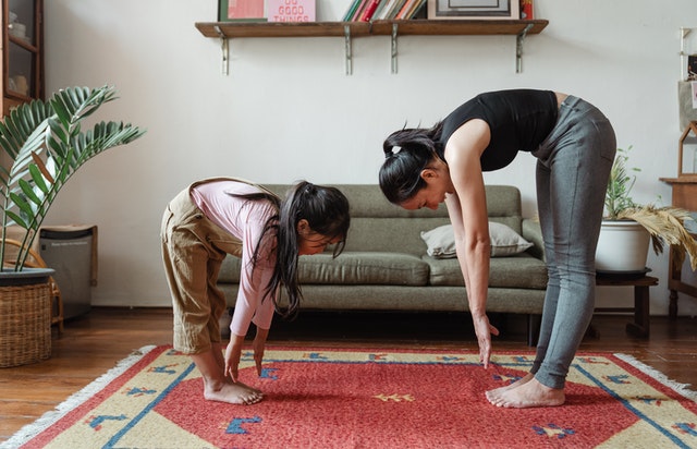 Girl and woman bend over to touch their toes while standing in a living room.