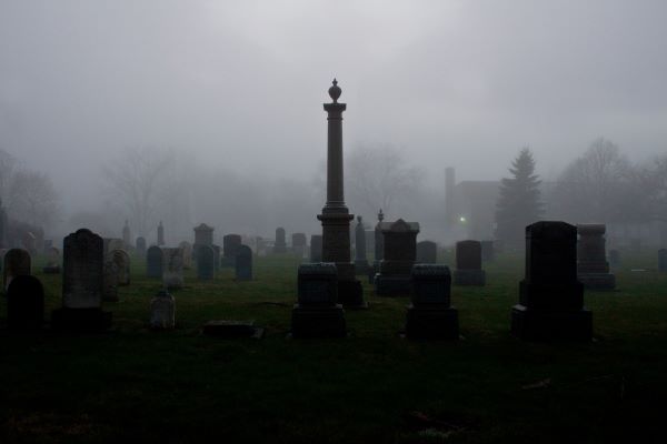 a monochromatic graveyard image in the fog with a tall gravestone marker