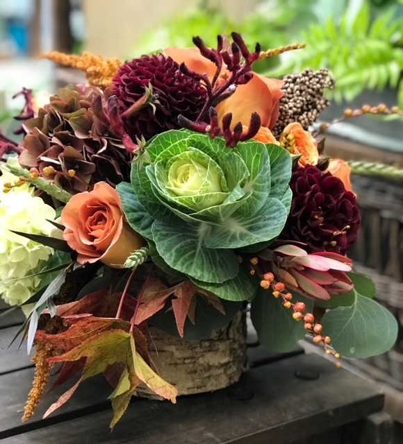 a fall floral arrangement that includes decorative cabbage, roses and fall leaves