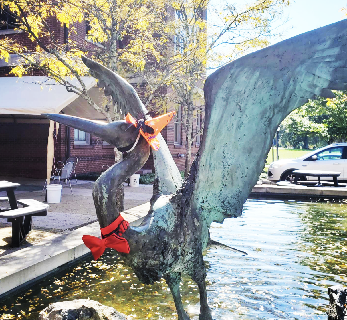 Sculpture of a heron in front of a fountain wearing a witch's hat and a bow tie.