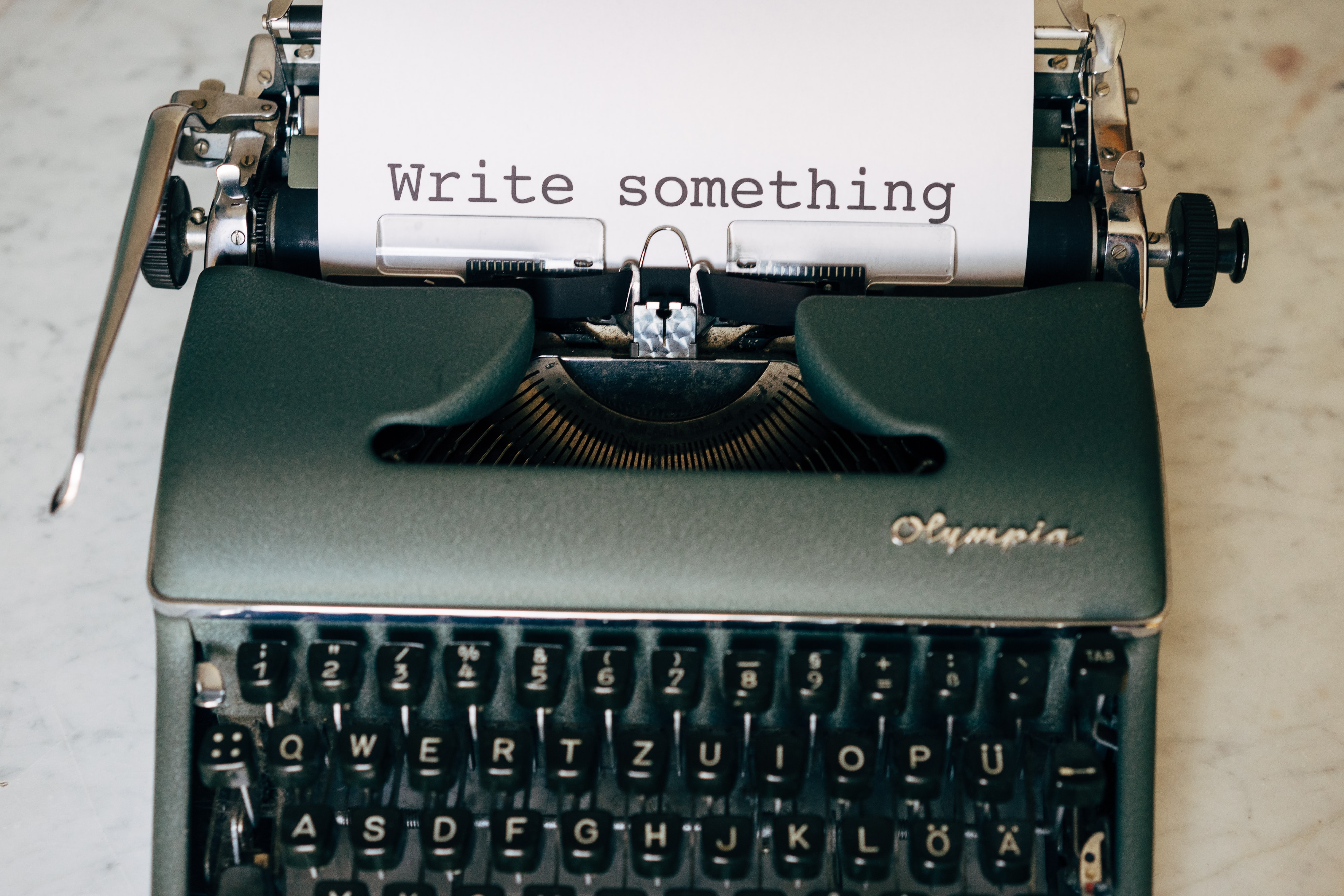 an old fashioned typewrite with a white piece of paper in it that says "write something"