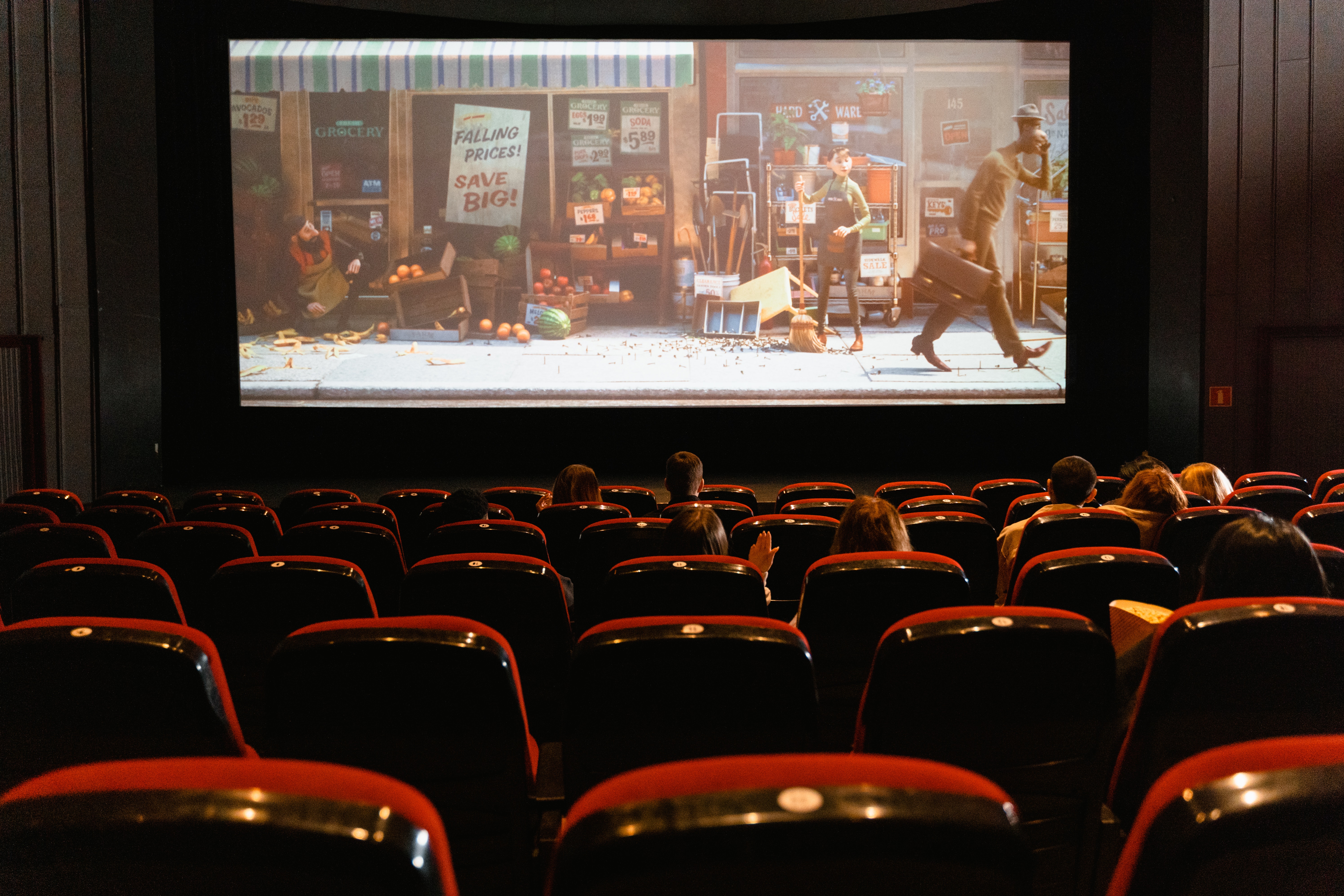 image of the inside of a movie theater, with plush red seats and a movie playing that is an old style storefront