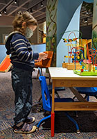 Child standing in front of a table with colorful toys on it. 