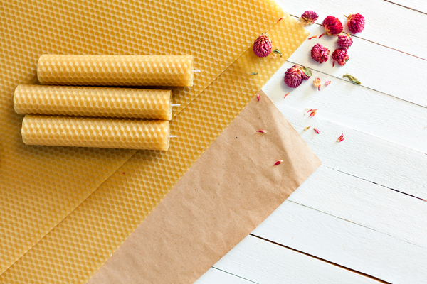 Three yellow beeswax candles resting on a sheet of yellow beeswax