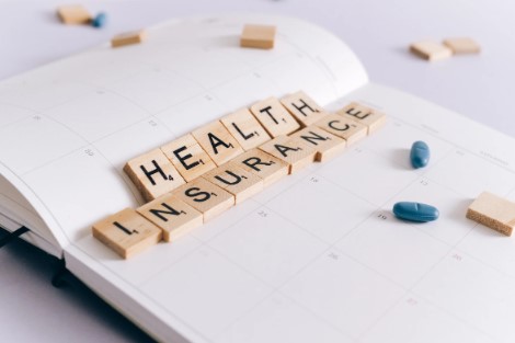 image of a medical chart with scrabble pieces that spell out health insurance, along with a few pills to boot