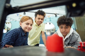Three children look at a 3D printer.