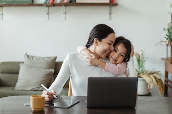 Child hugging mother from behind while she is working at a laptop.