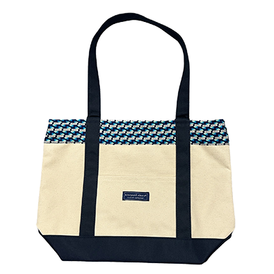 A Vineyard vine canva bag with dark blue bottom and handles. The top is exclusive fabric with the 1894 Day logo on it in a repeating pattern.