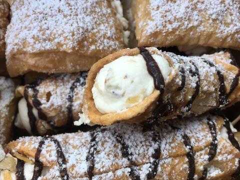 Stack of cannoli pastries with powdered sugar and drizzled chocolate
