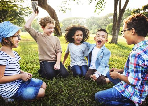 Group of five children laughing on grass