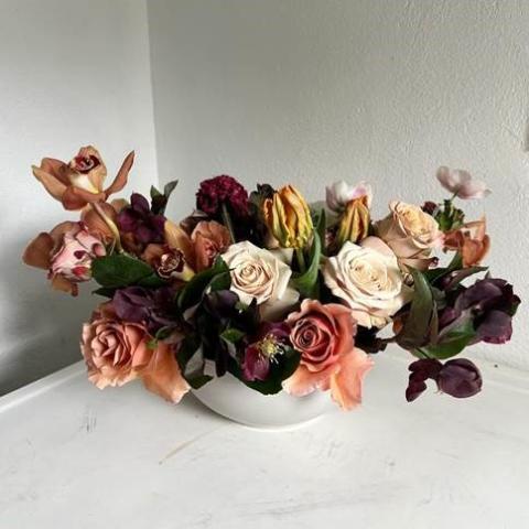 Flower arrangement in a white vase with white background. Assortment of flowers of different varieties and colors including peach, burgundy, and cream.