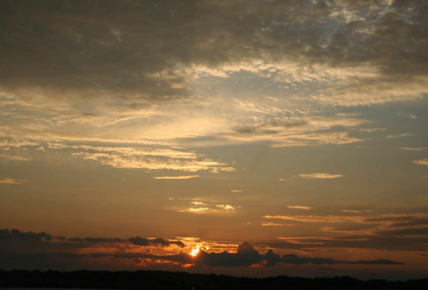 Setting sun in the horizon with a cloudy sky and dark background