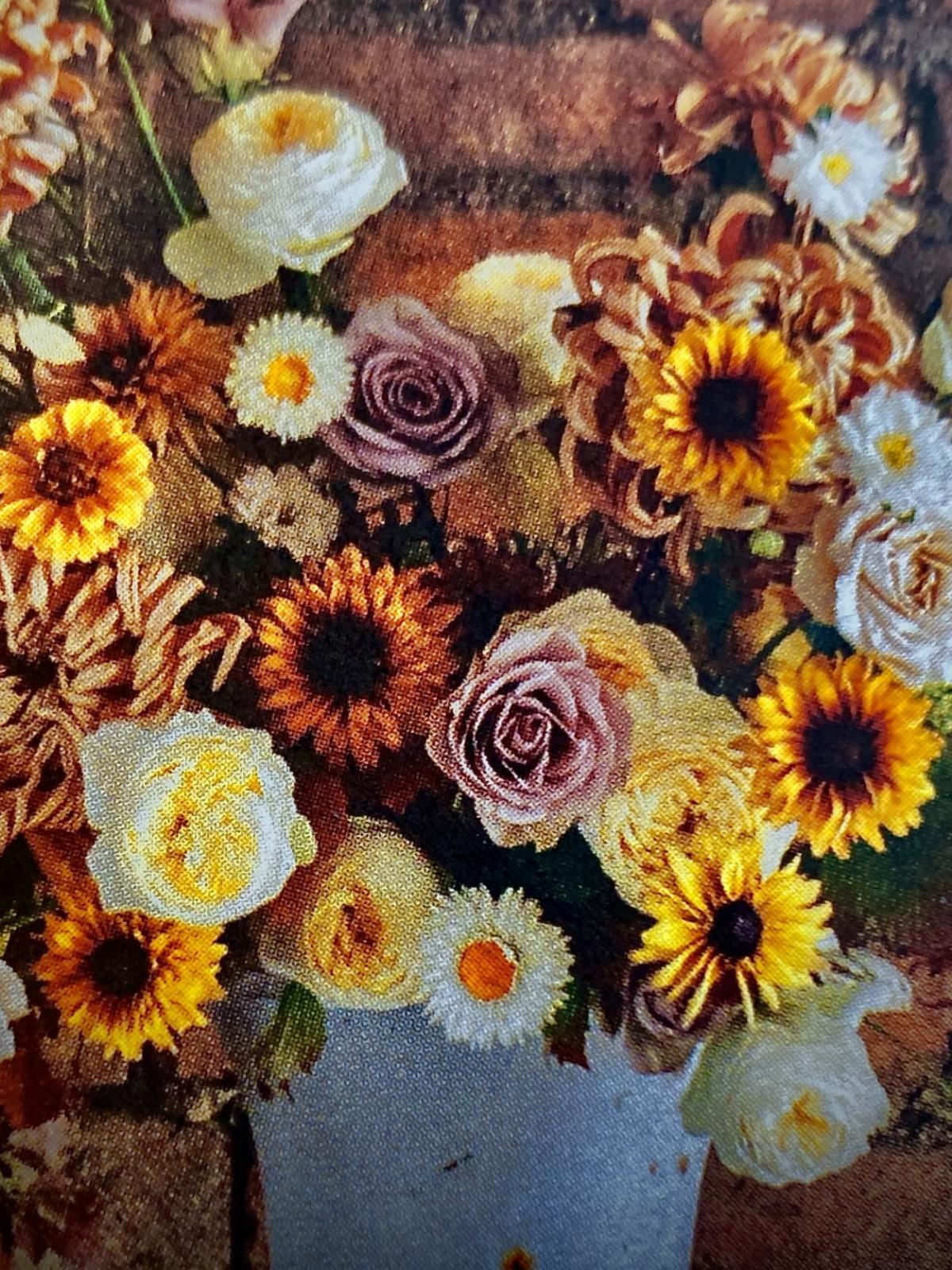 A metal bucket filled with sunflowers, daisies, and yellow, purple and white roses. 