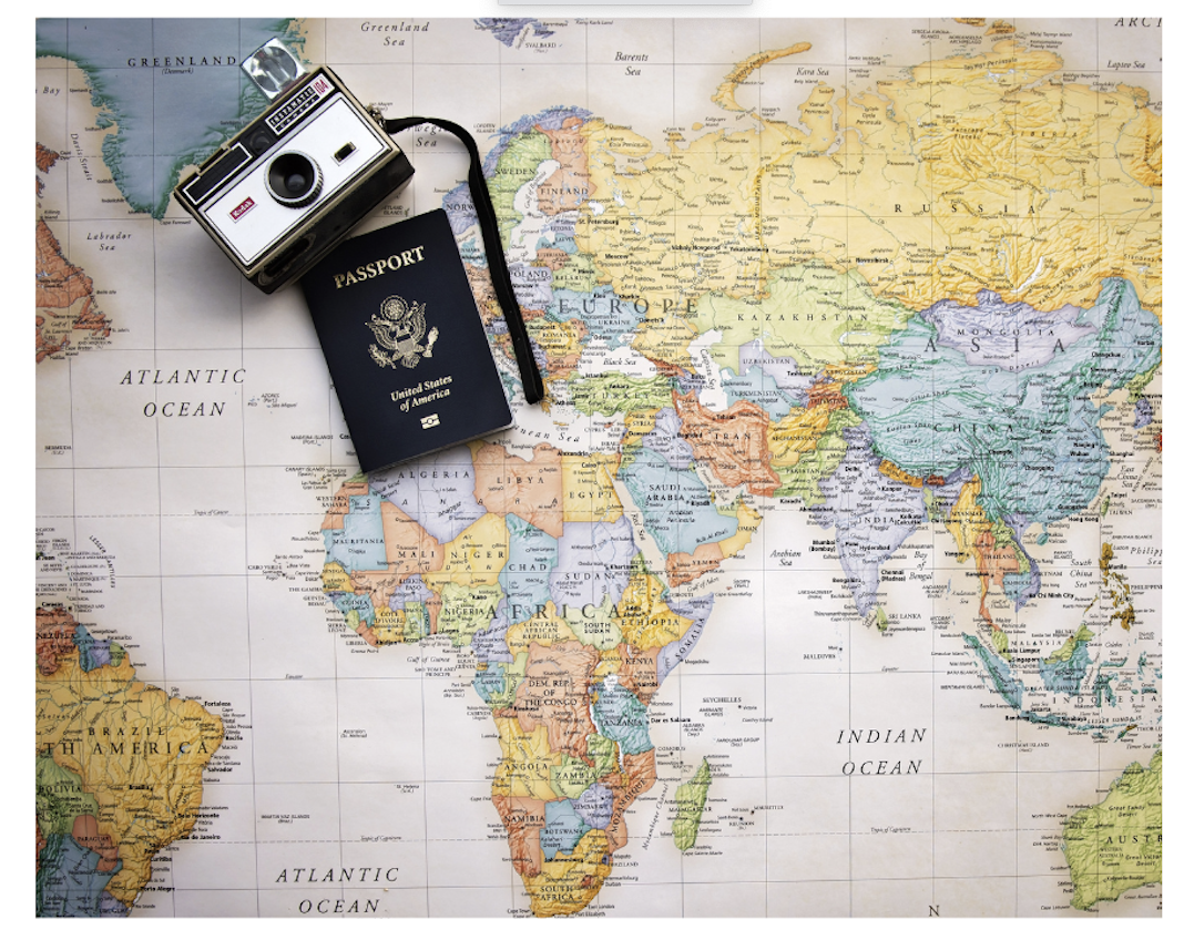 A colorful map of the world with an American passport and camera lying on top.