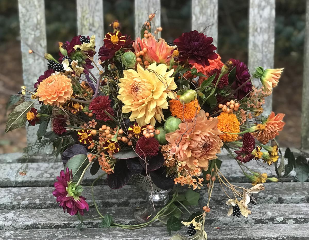 Yellow, orange, peach, and maroon dahlias of varying sizes, overflowing in a container.