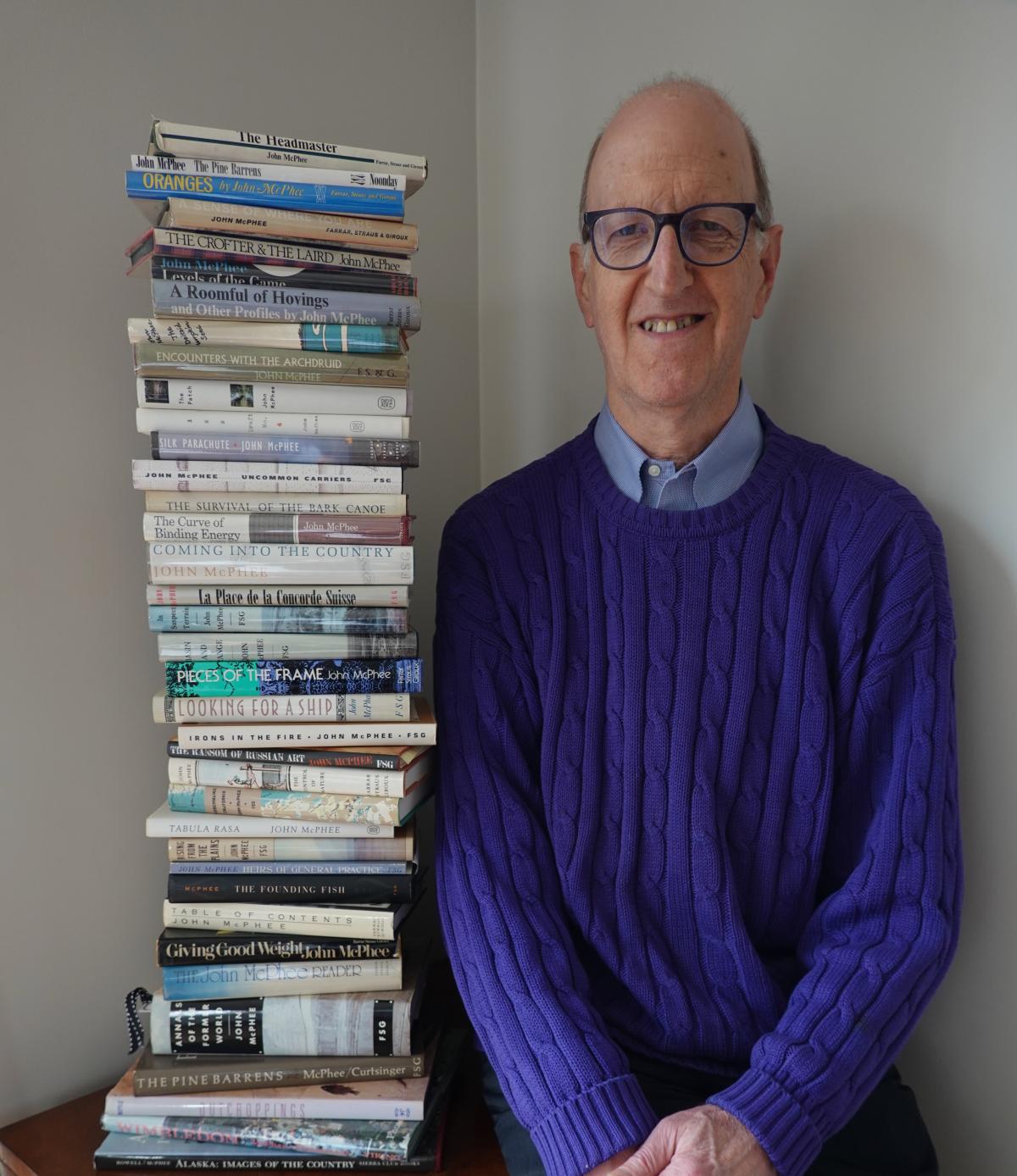 Author Noel Rubinton with a large stack of books written by John McPhee